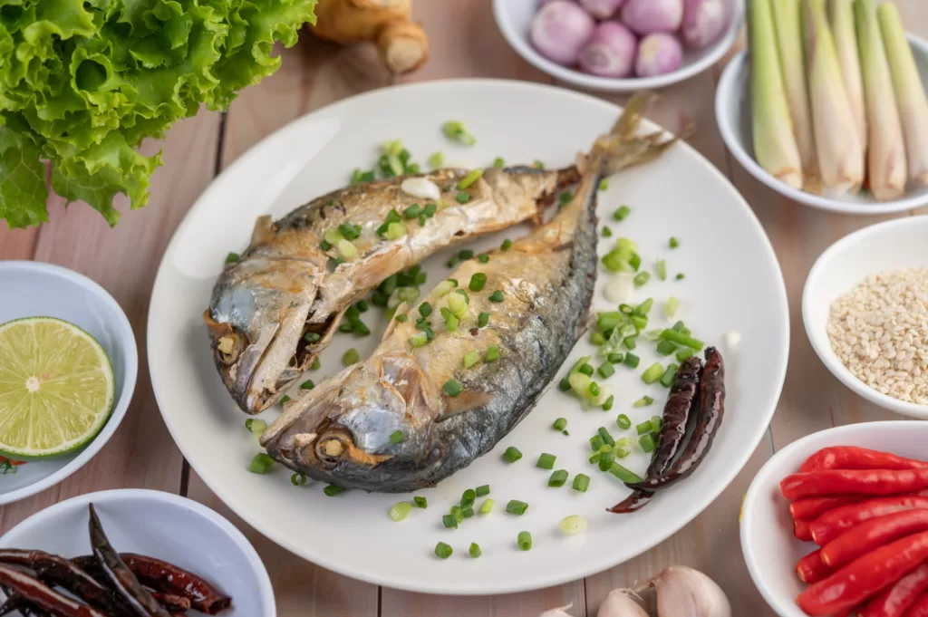 two cooked mackerel placed white dish sprinkled with spring onions
